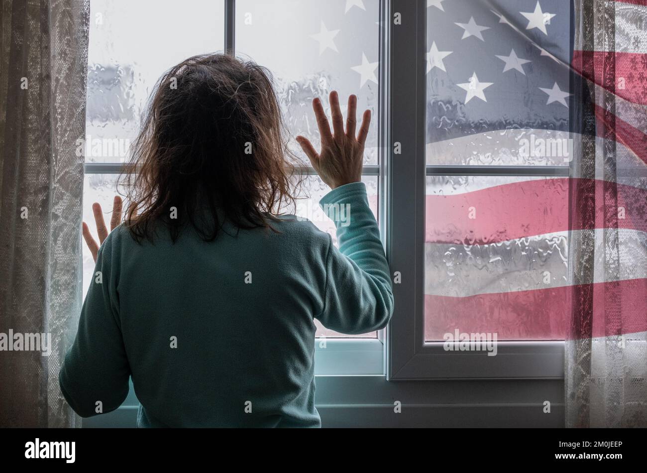 Frau am Fenster an Regentagen. Die US-Flagge außen. Bild: Weibliche Depression, häusliche Misshandlung, Menschenhandel, häusliche Gewalt, Psychische Gesundheit... Stockfoto