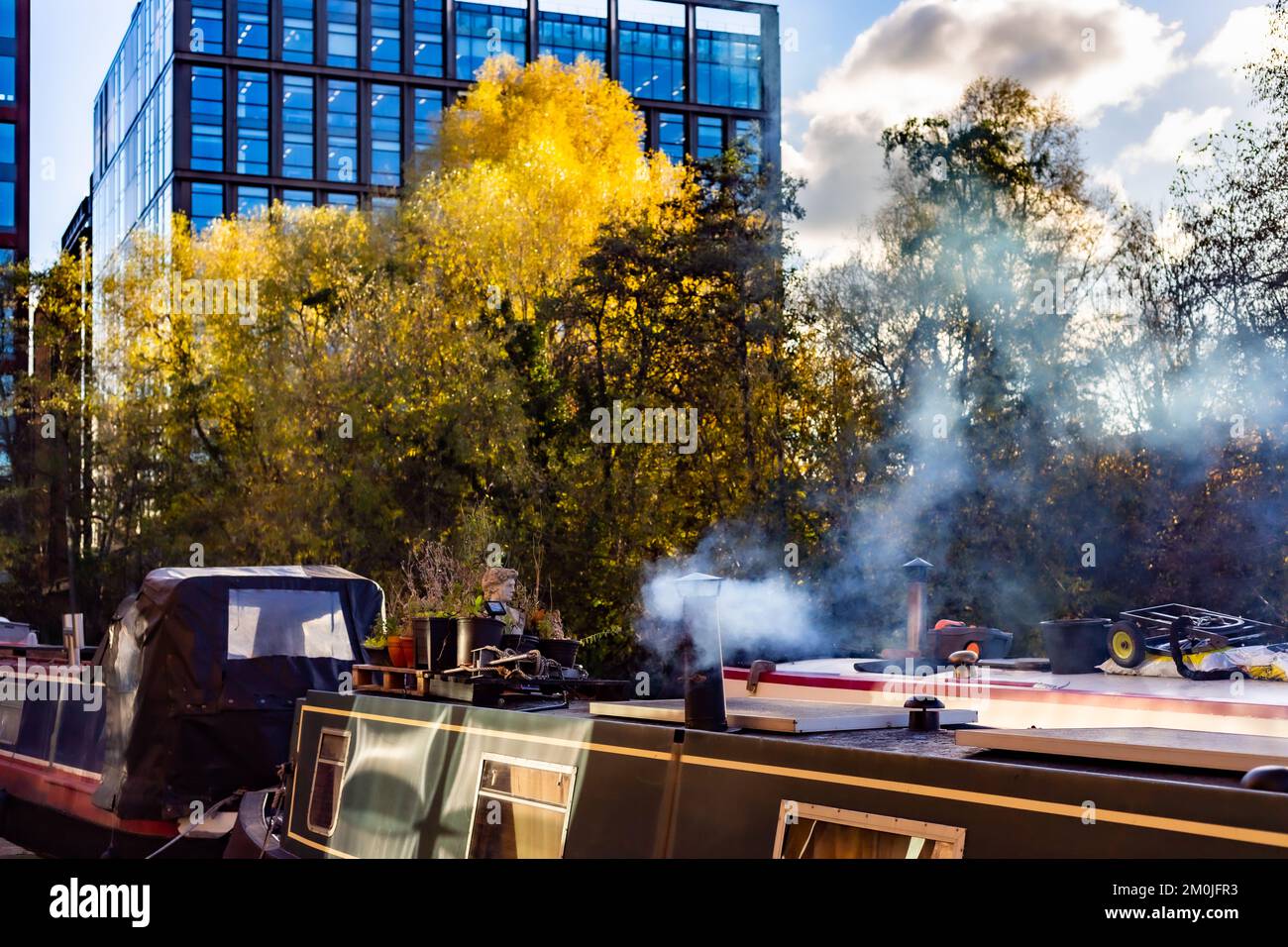 Kanalboote, die auf dem Kanal bei King's Cross festgemacht sind. Zwei Kanalboote, die mit starker Seitenbeleuchtung fotografiert wurden. Ein Boot hat einen Kamintrichter, der raucht. Stockfoto