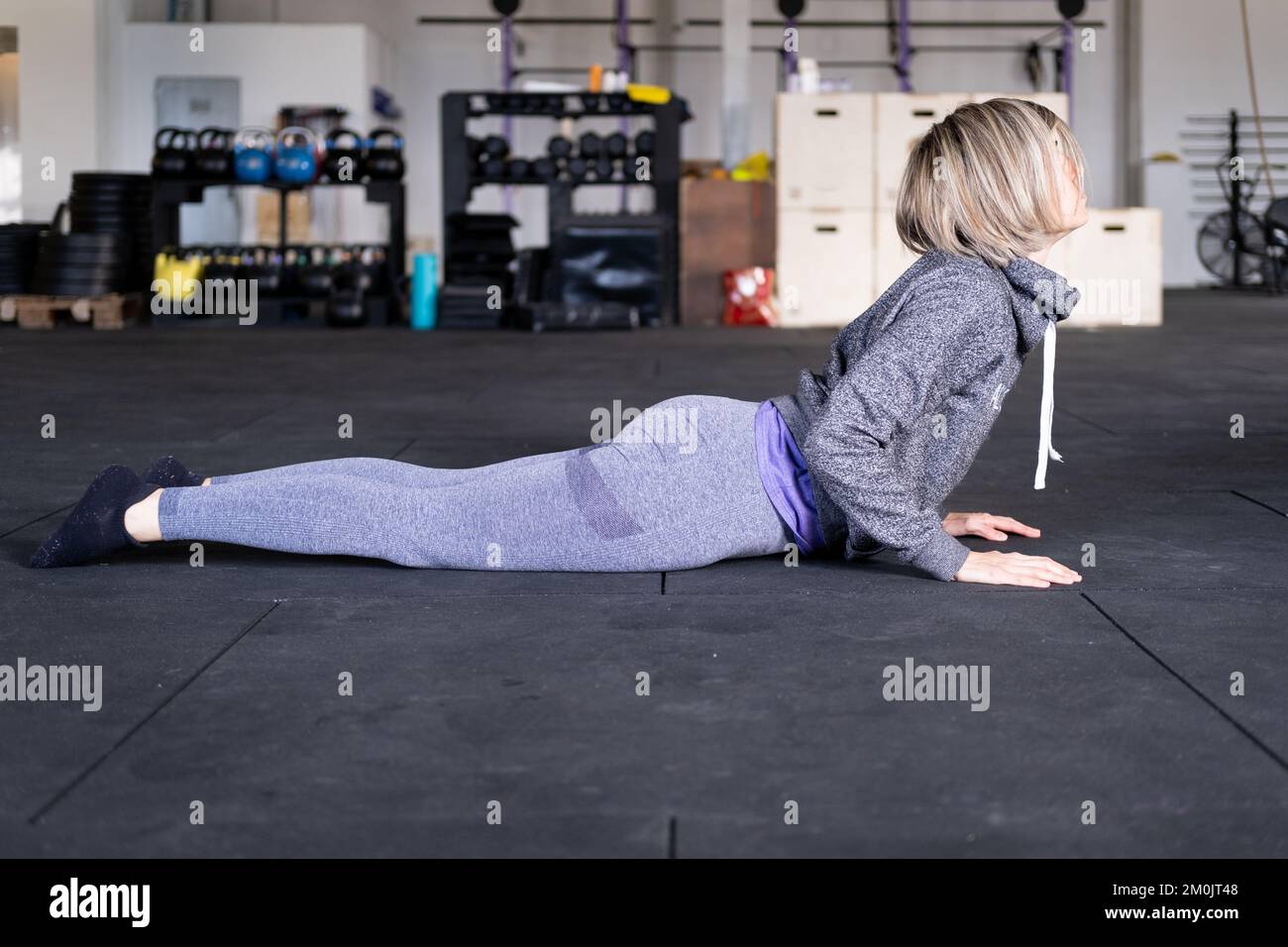 Eine blonde, mittelErwachsene Frau, die als Teil ihres Vinyasa-Flow-Yoga-Trainings allein eine nach oben gerichtete Hundehaltung einnimmt und Sportbekleidung im Fitnessstudio trägt. Stockfoto