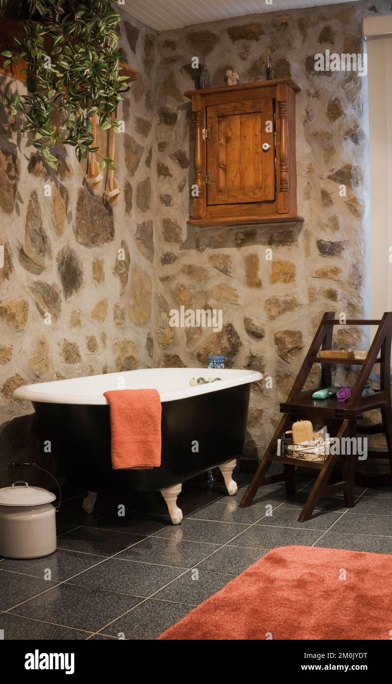 Schwarz-weiße freistehende Badewanne und antike Möbel im Badezimmer im Nachbau des alten Canadiana Cottage-Stil Holz- und Feldsteinhauses. Stockfoto