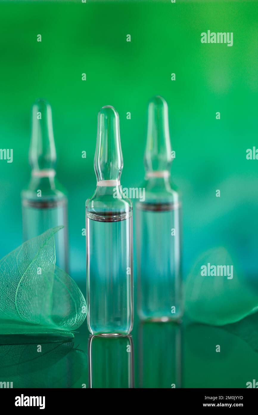 Mesotherapie und Dermabrasionsserum in Ampullen. Kosmetische Ampullen. Schönheitsprodukt. Transparente Ampullen und grüne, skelettierte Blätter auf türkisfarbenem Stockfoto