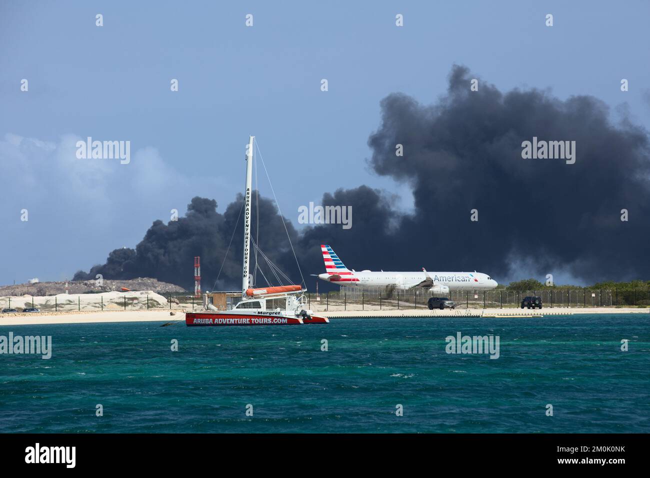 ORANJESTAD, ARUBA - 07. APRIL 2022: Flugzeug verlässt Queen Beatrix Airport, während Müll auf dem Serlimar Mülldeponie in Oranjestad auf Aruba verbrannt wird Stockfoto