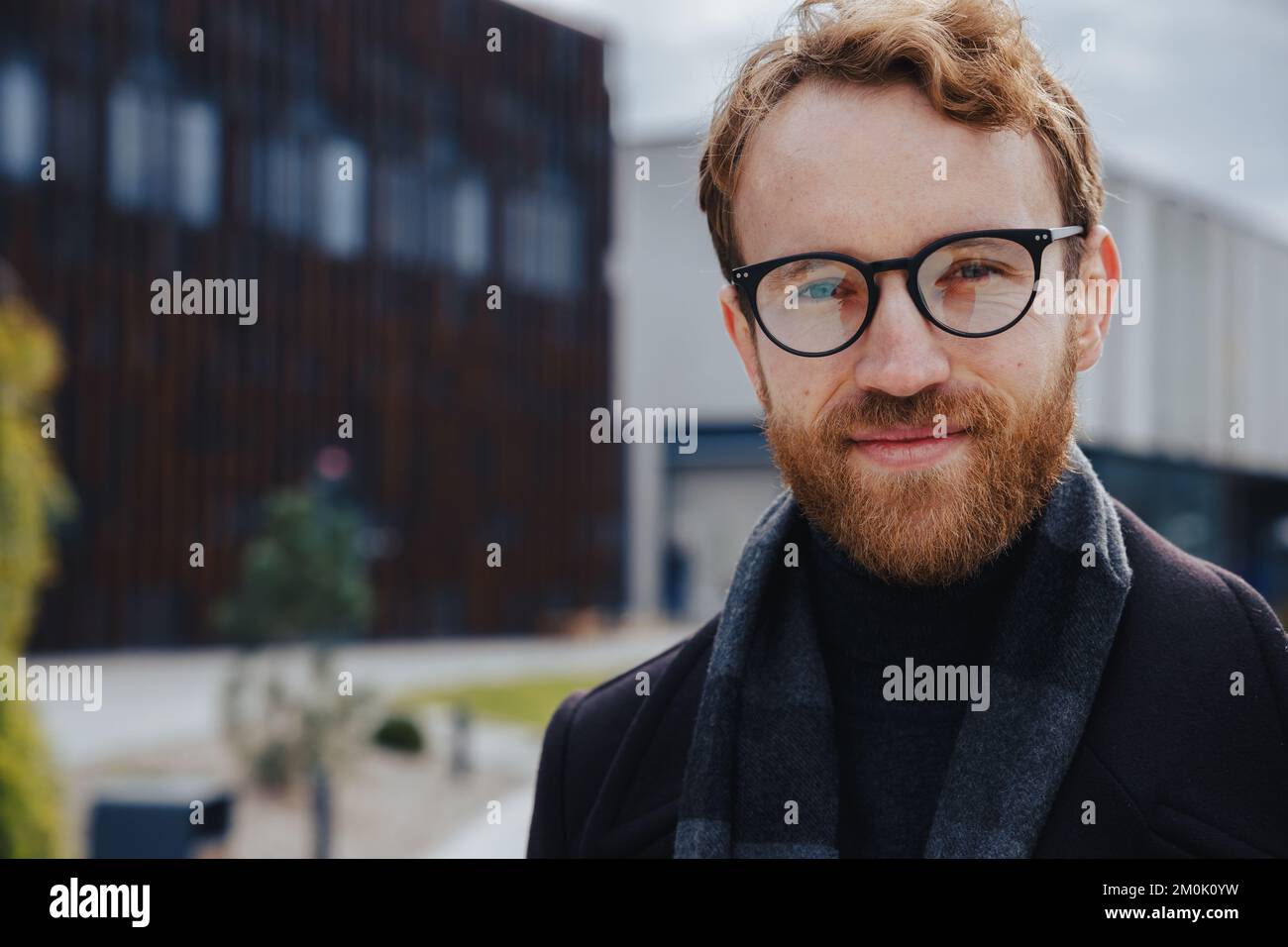 Ein junger rothaariger Typ, ein Geschäftsmann mit Brille, schaut in die Kamera vor dem Hintergrund eines urbanen Stils. Nahaufnahme des Porträts Stockfoto