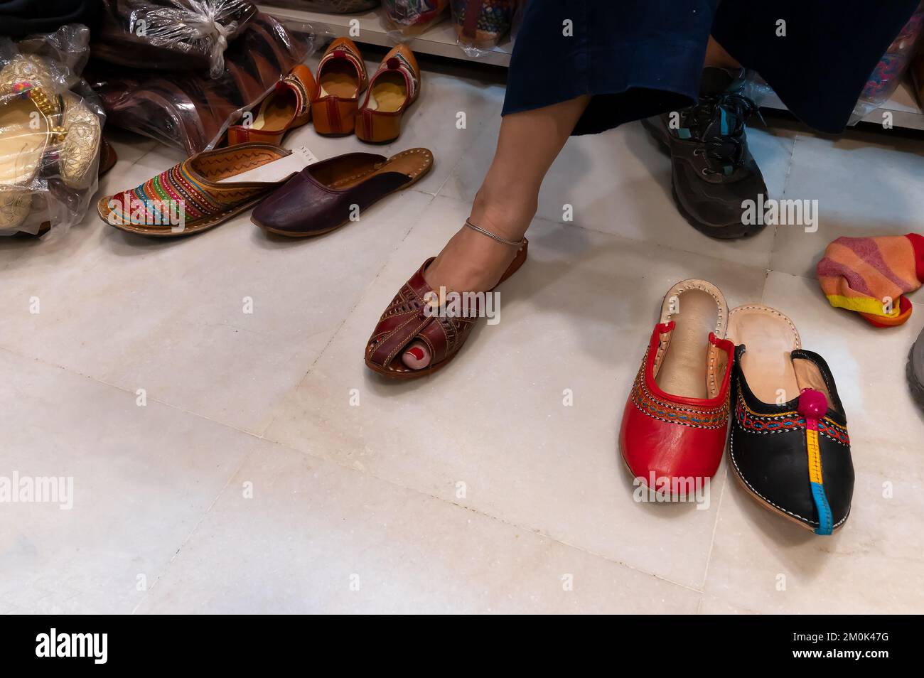 Schöne indische Frau, die ihren Fuß für das Anbringen von bunten Rajsathani Damenschuhen im Schuhgeschäft am berühmten Sardar Market und Ghanta Ghar Clock probiert Stockfoto