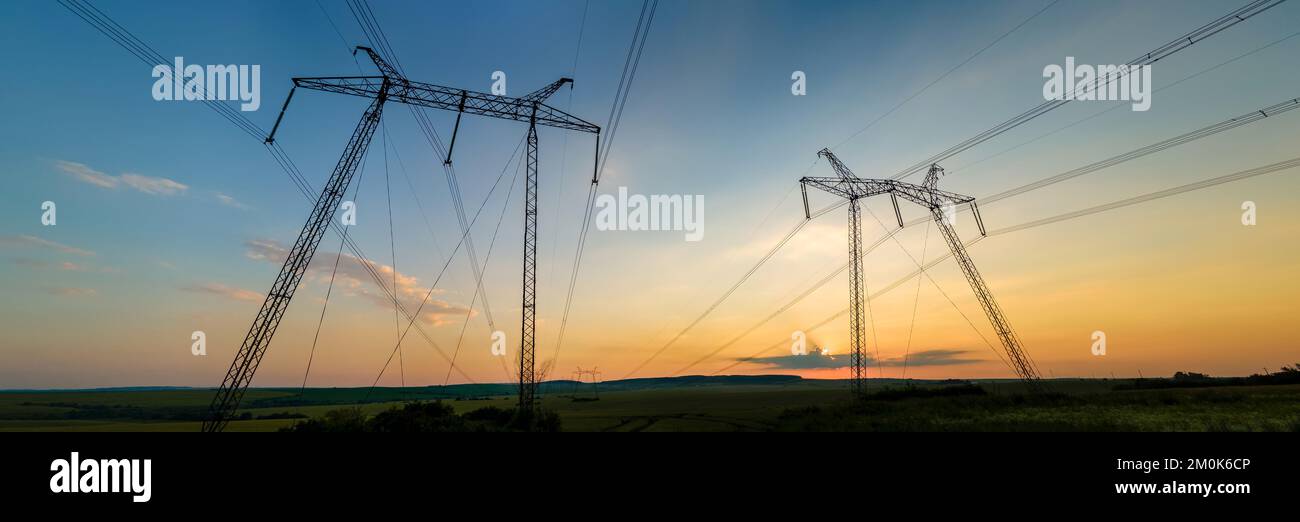 Dunkle Silhouette von Hochspannungstürmen mit Stromleitungen bei Sonnenaufgang Stockfoto