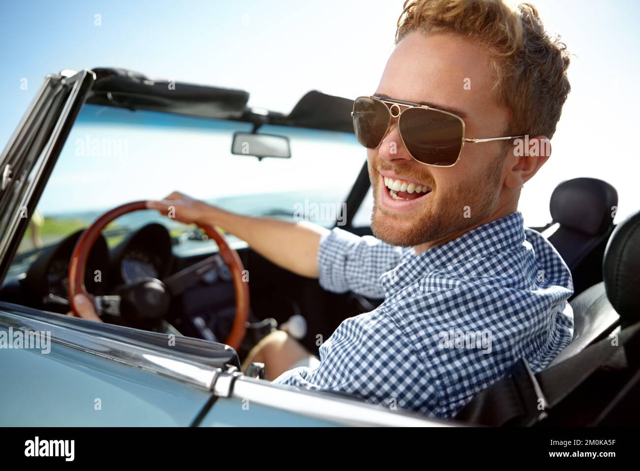 In diesem Auto sieht es einfach cool aus. Ein attraktiver junger Mann, der an einem sonnigen Nachmittag in seinem Cabrio fährt. Stockfoto