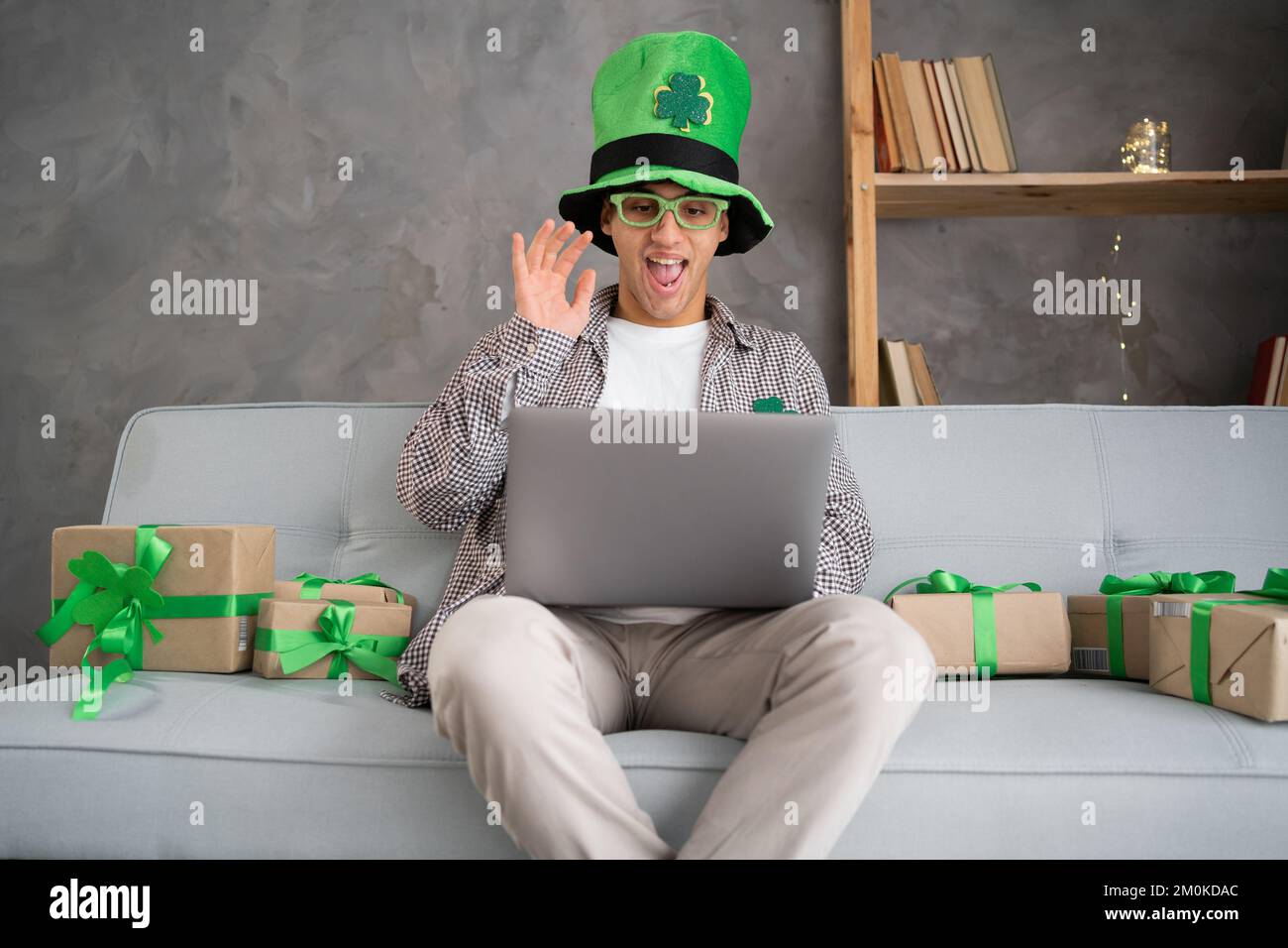 Junger Mann mit Leprechaun hat Video, Freunde auf dem Laptop anrufen, Familie per Webcam begrüßen, Geschenkbox von St. Patrick's Day im virtuellen Online-Chat Meeti öffnen Stockfoto