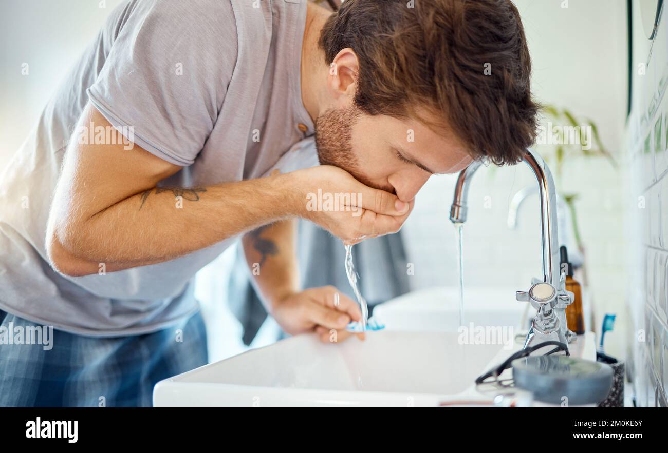 Ein hübscher Mann, der sich zu Hause in einem Badezimmer den Mund spült. Kaukasischer Mann mit Mundwasser für frischen Atem in seiner Wohnung Stockfoto