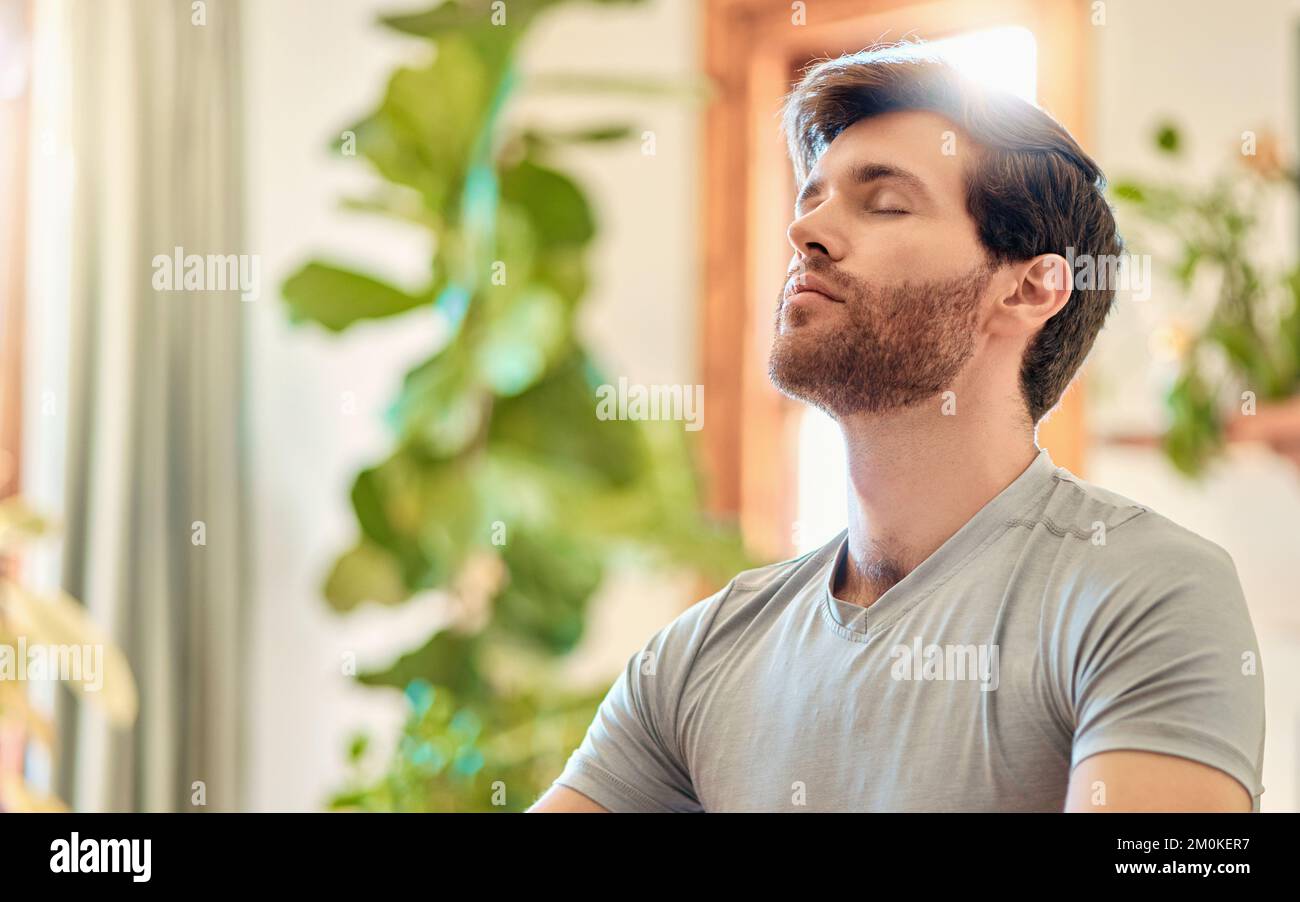 Ein junger weißer Mann atmet tief ein, während er zu Hause Yoga praktiziert und in Harmonie meditiert. Das Gesicht eines ruhigen, entspannten und konzentrierten Mannes Stockfoto