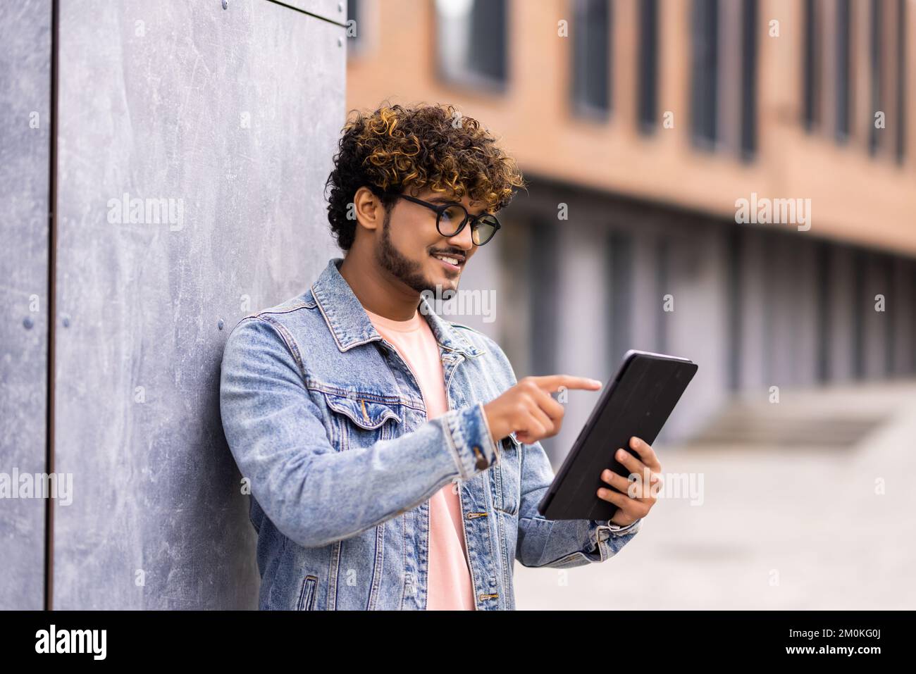 Ein gutaussehender Mann, der in einer Stadt ein digitales Tablet benutzt. Schüler lesen draußen. Stockfoto