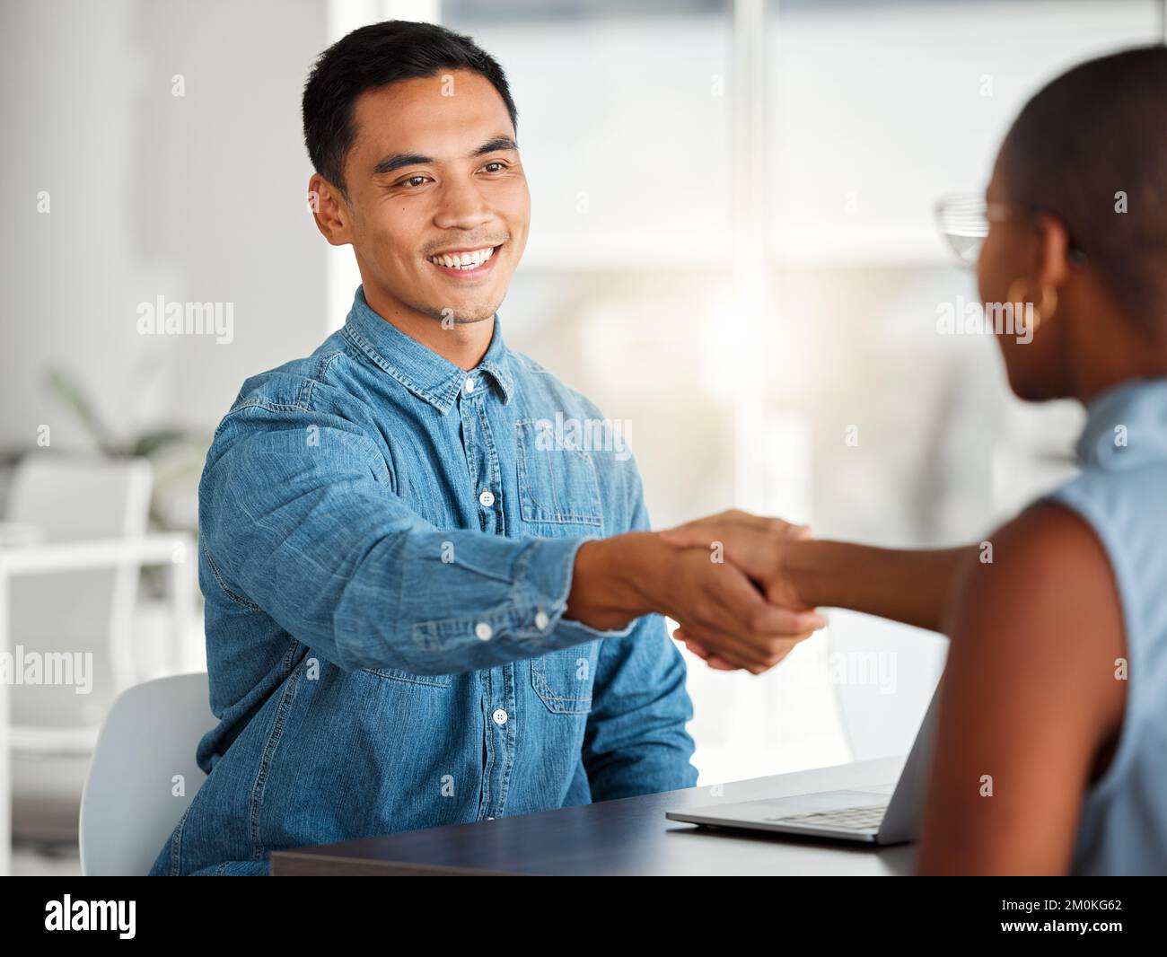 Zwei fröhliche Geschäftsleute, die sich bei einem Interview bei der Arbeit die Hand schütteln. Fröhliche Kollegen, die im Büro mit einem Händedruck begrüßt werden. Asiatischer männlicher Boss Stockfoto