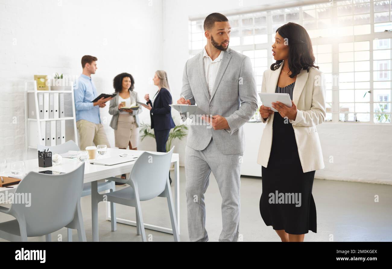Gemischter Geschäftsmann und afroamerikanische Geschäftsfrau, die sich unterhalten, während sie ein digitales Tablet in einem Büro mit Kollegen verwenden. Geschäftsleute arbeiten Stockfoto