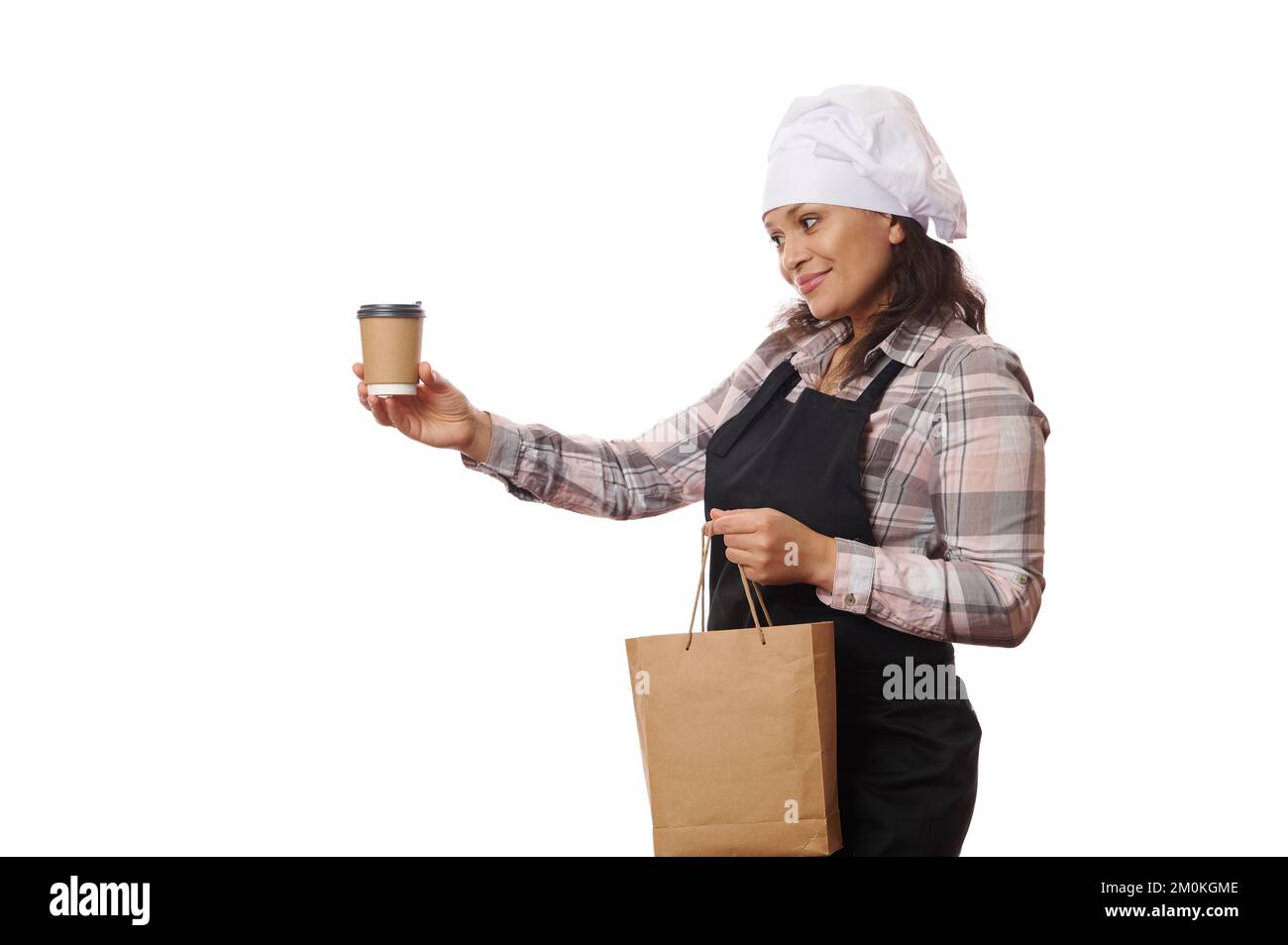 Hübsche Kellnerin mit Kochmütze und Schürze, verkauft heißen Kaffee zum Mitnehmen in Einweg-Pappbecher, weißer Hintergrund Stockfoto