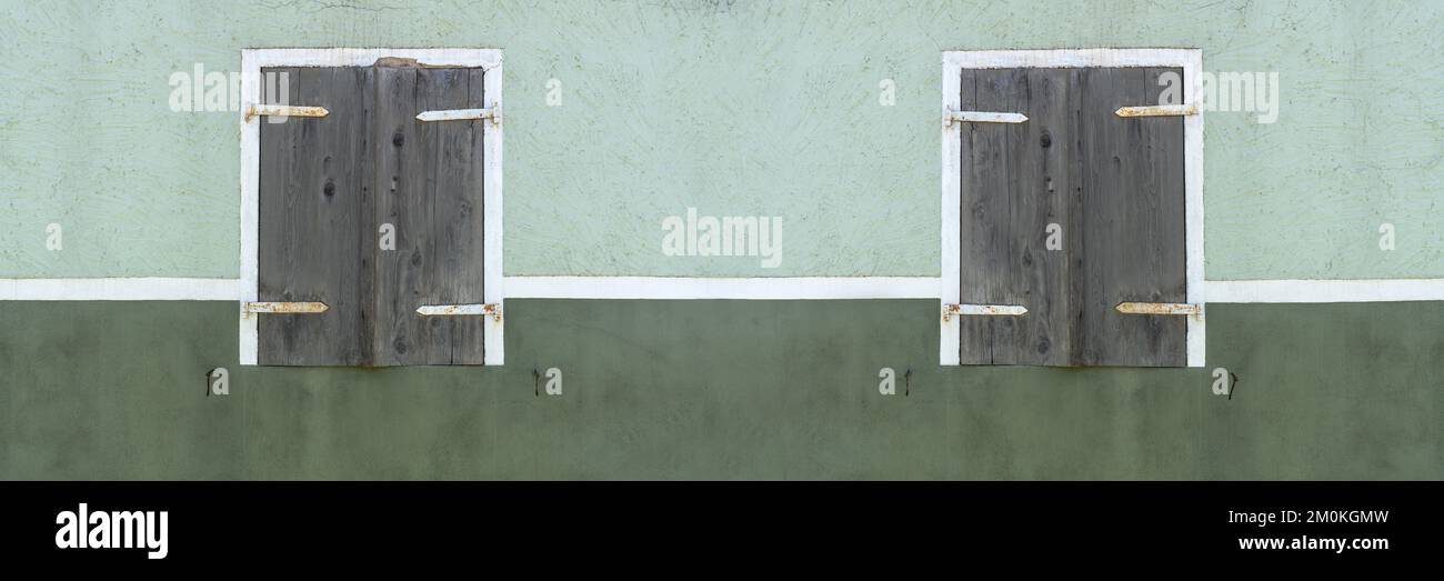 Zwei alte Fenster mit geschlossenen Fensterläden in einer grün-weißen Fassade Stockfoto