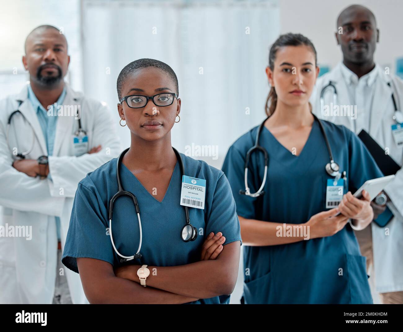 Gruppe von verschiedenen ernsthaften Ärzten stehen mit gekreuzten Armen während der Arbeit in einem Krankenhaus. Fachkundige Mediziner, die auf die Arbeit fokussiert sind Stockfoto