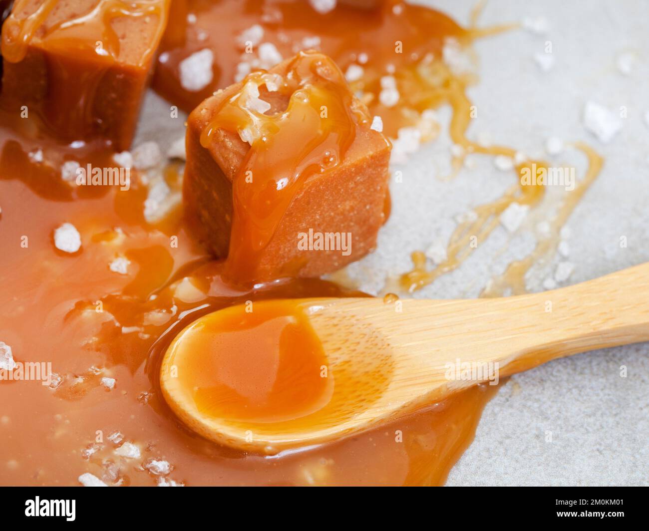 Gesalzenes Karamell, ein Geschmacksempfinden. Grobe Salz- und Karamellblöcke mit einer klebrigen, cremigen, gesalzenen Karamellsauce auf Grau Stockfoto