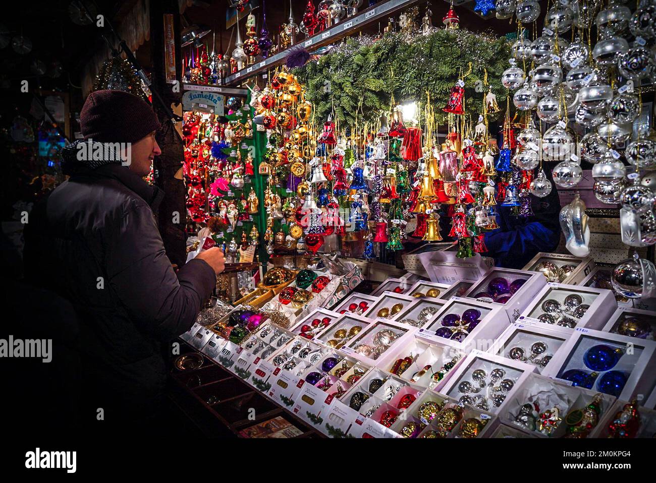 Ein Mann sieht nachts auf einem Weihnachtsmarkt in München auf eine Theke mit Silvesterspielzeug Stockfoto