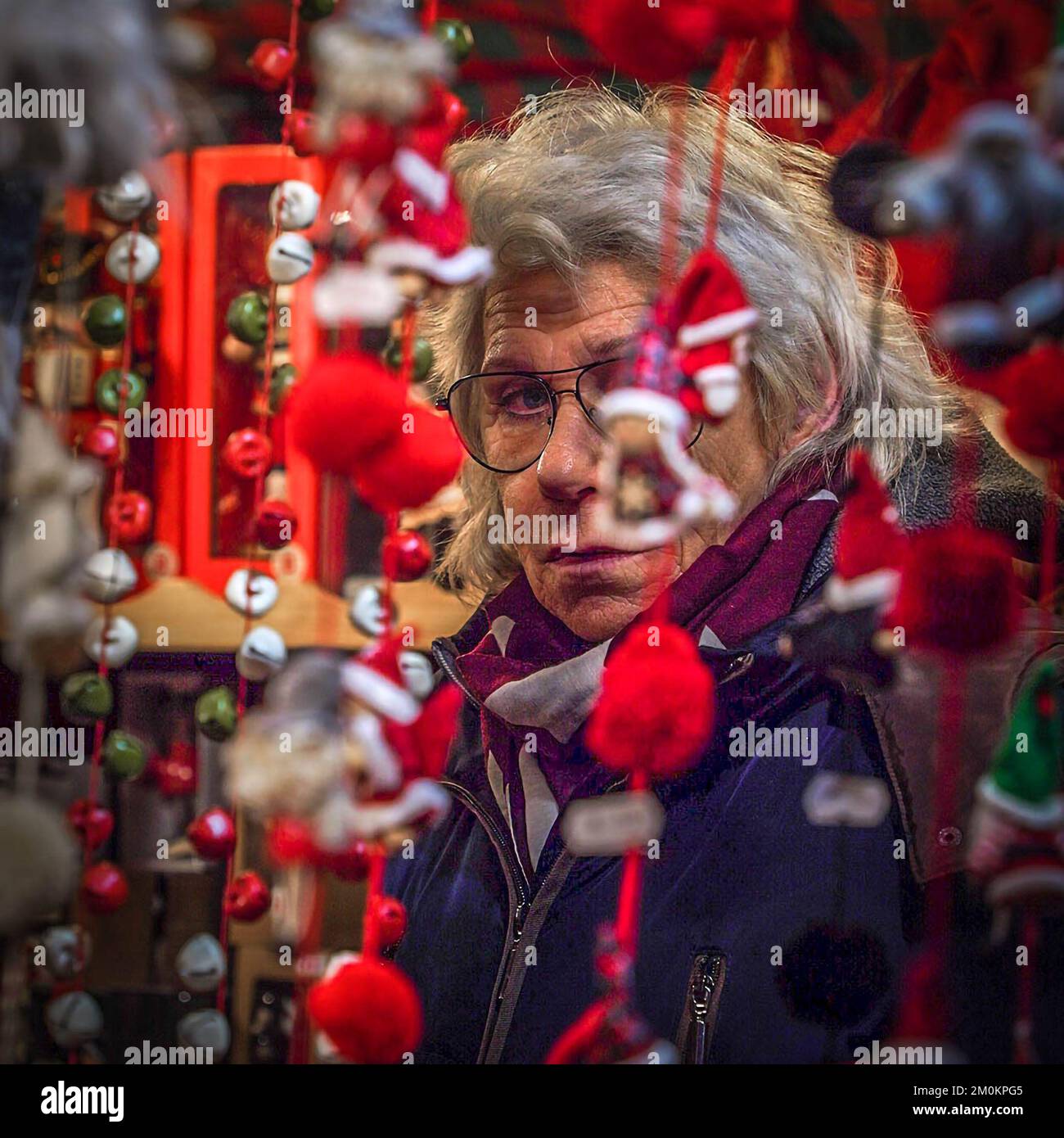 Eine müde, reife Verkäuferin steht nachts auf einem Weihnachtsmarkt in München hinter dem Neujahrsspielzeug Stockfoto