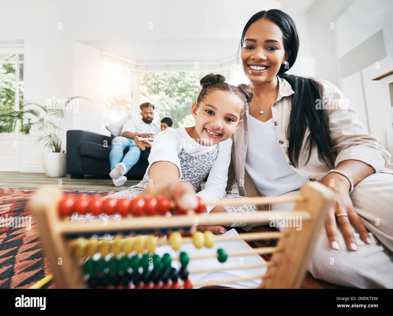 Die hispanische Mutter sitzt zu Hause im Ausfallschritt auf dem Boden und lächelt mit ihrer Tochter, während sie mit Lernspielzeug spielt. Liebenswert kleines Mädchen spielen Stockfoto