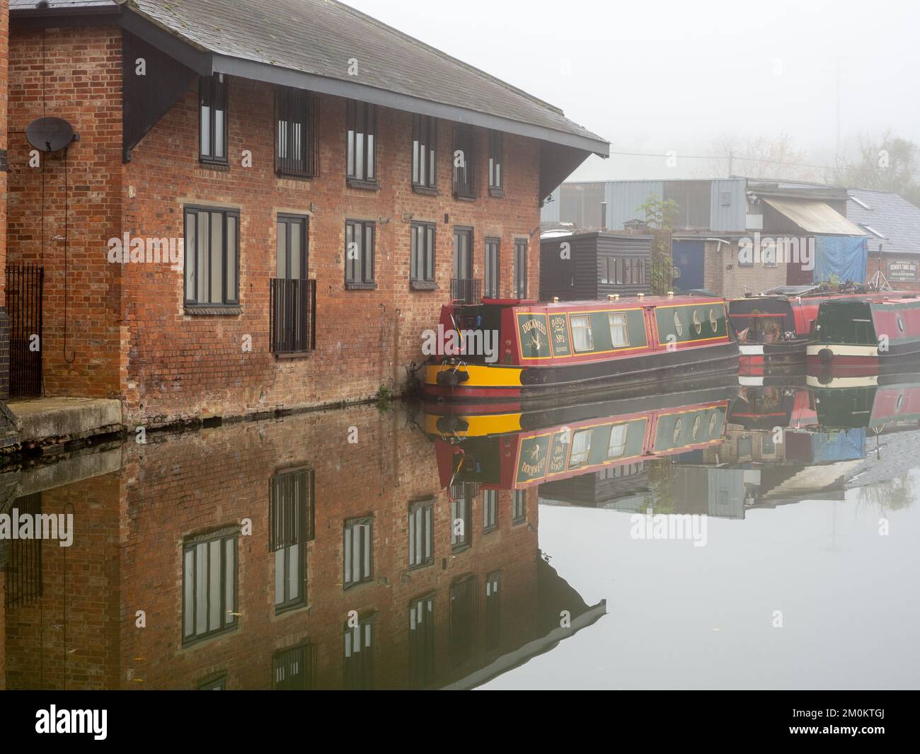 Ein kalter nebeliger Wintermorgen auf dem Canal Grand Union, Blisworth, Northamptonshire, Großbritannien; mit einer alten cornmill, die jetzt in Wohnungen umgewandelt wurde. Stockfoto