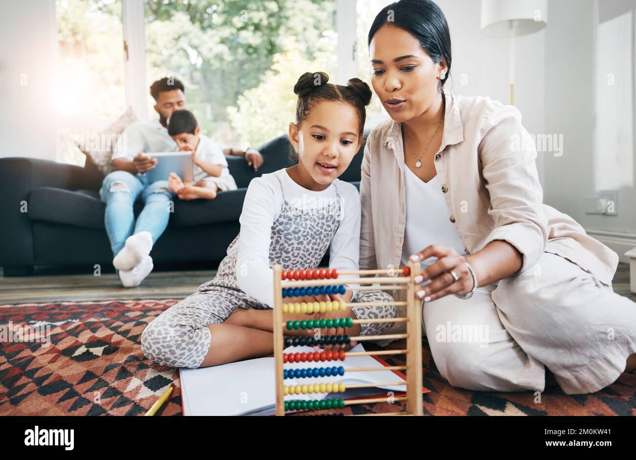 Die hispanische Mutter sitzt zu Hause im Ausfallschritt auf dem Boden und lächelt mit ihrer Tochter, während sie mit Lernspielzeug spielt. Liebenswert kleines Mädchen spielen Stockfoto