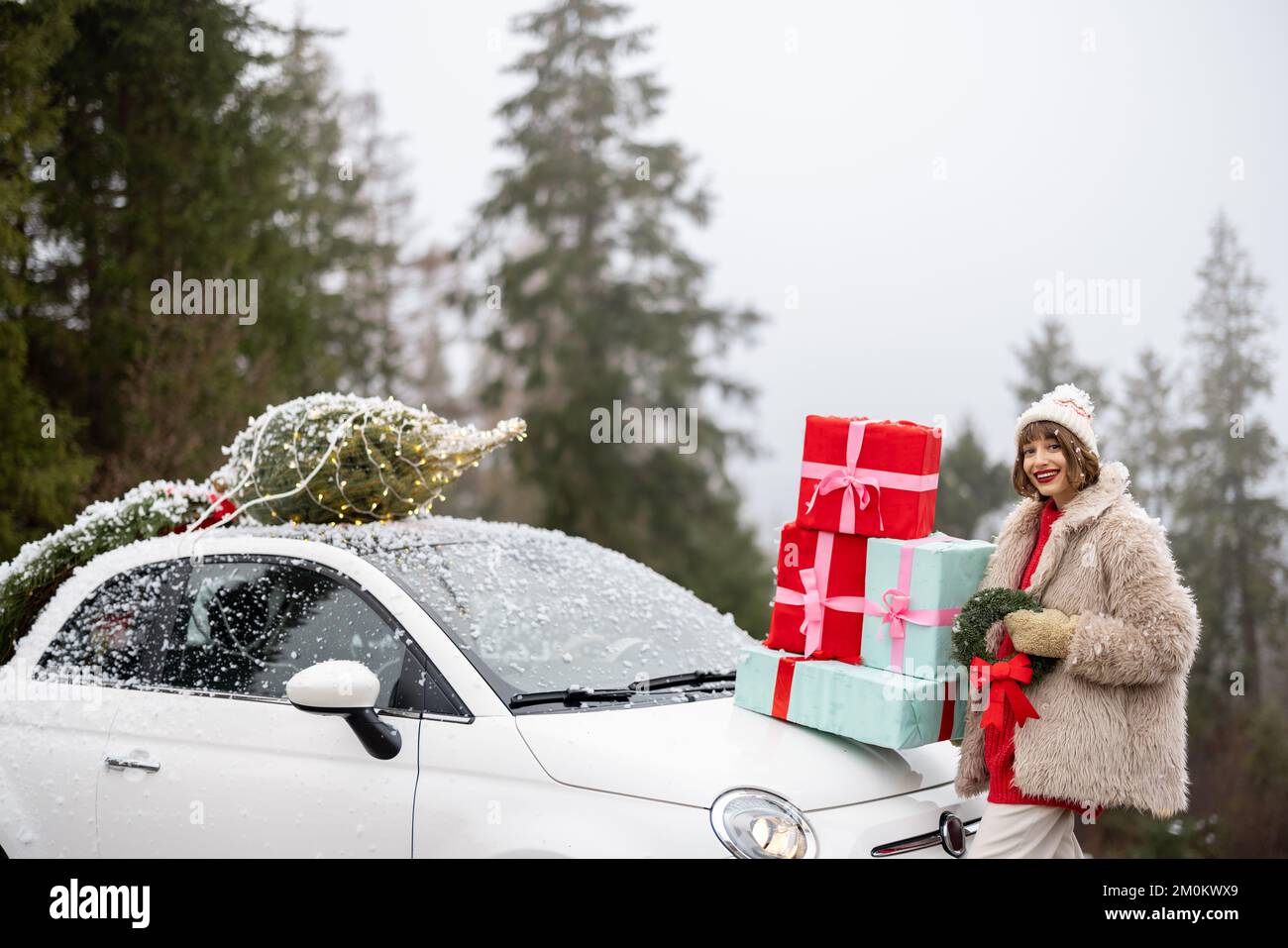 Weihnachtsfotokarte einer Frau mit Geschenken und Auto in den Bergen bei Schneewetter Stockfoto