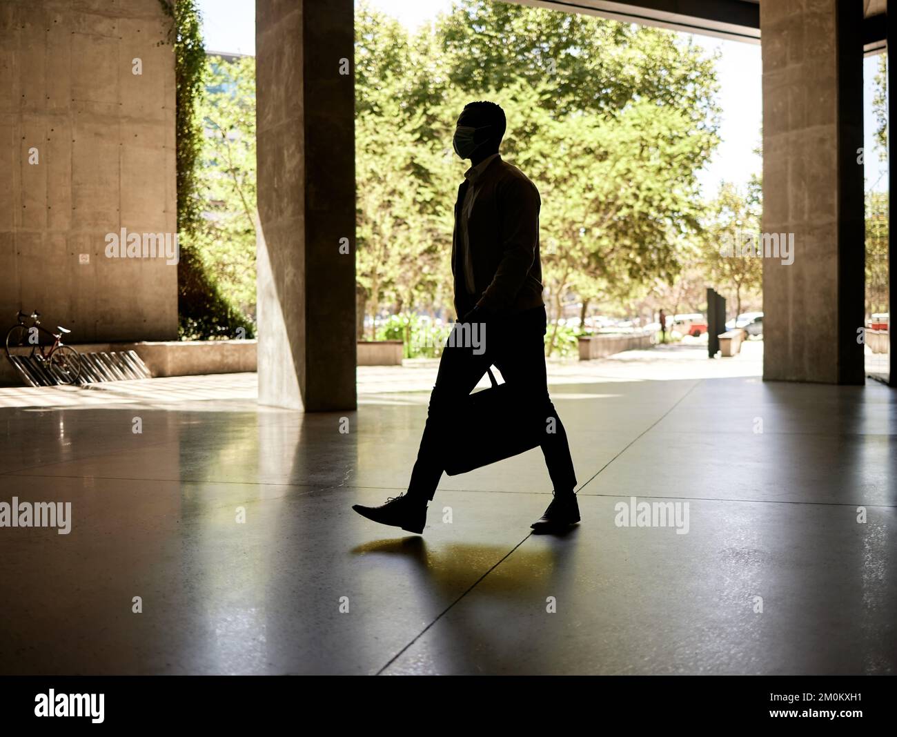 Silhouette eines Geschäftsmanns, der morgens auf dem Weg zur Arbeit in einem Bahnhof unterwegs ist, während er seine Tasche trägt Stockfoto