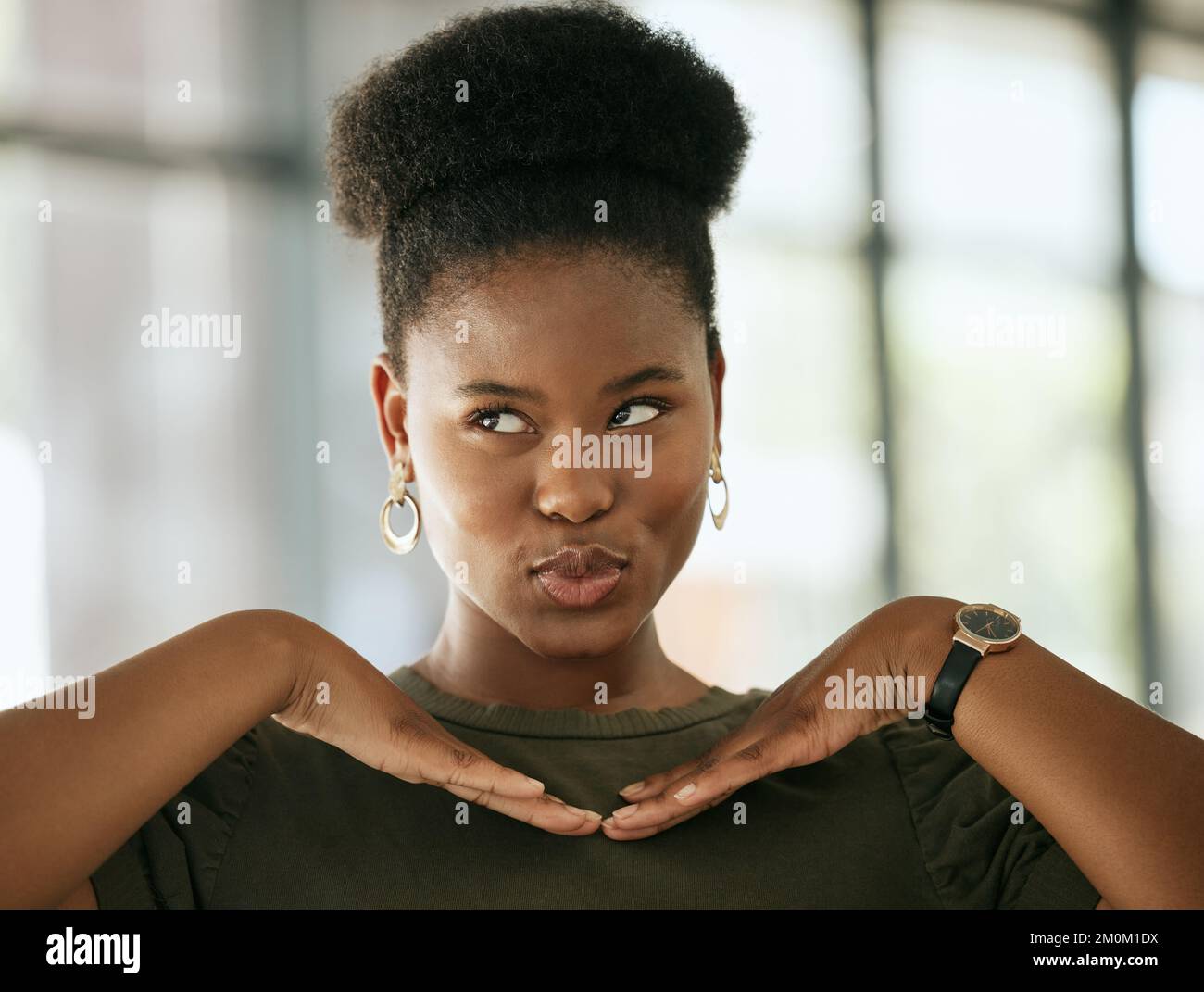 Glückliche afroamerikanische Geschäftsfrau posierte mit den Händen unter dem Gesicht, während sie schmollte und in einem Büro wegschaute. Verspielte Unternehmerin Stockfoto