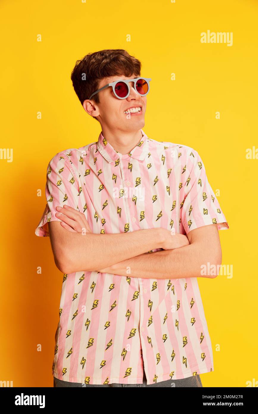 Porträt eines verblüfften jungen Mannes in modischer Brille, die isoliert auf hellgelbem Hintergrund lächelt. Jugendkultur, positive Emotionen Stockfoto