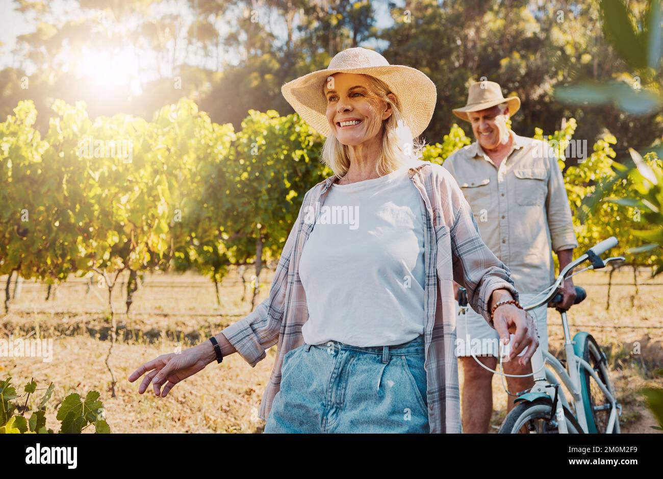 Lächelndes Seniorenpaar, das zusammen auf dem Weinberg zusammenläuft. Glücklicher kaukasischer Ehemann und Ehefrau schieben Fahrrad, während sie den Tag auf der Farm danach genießen Stockfoto