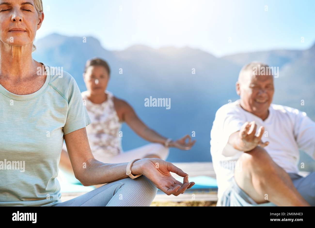 Ältere Männer und Frauen sitzen in Lotusposition und üben Meditation während Yoga-Bewegung in der Natur und fühlen sich ruhig. Rentner leben gesund Stockfoto