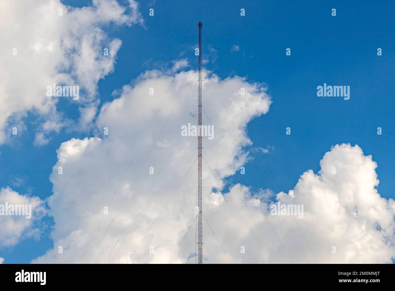 Eine Radioantenne aus einem Stahlrahmen befindet sich in der Bildmitte mit einem am Boden befestigten Seil. Der Hintergrund ist ein hellblauer Himmel Stockfoto