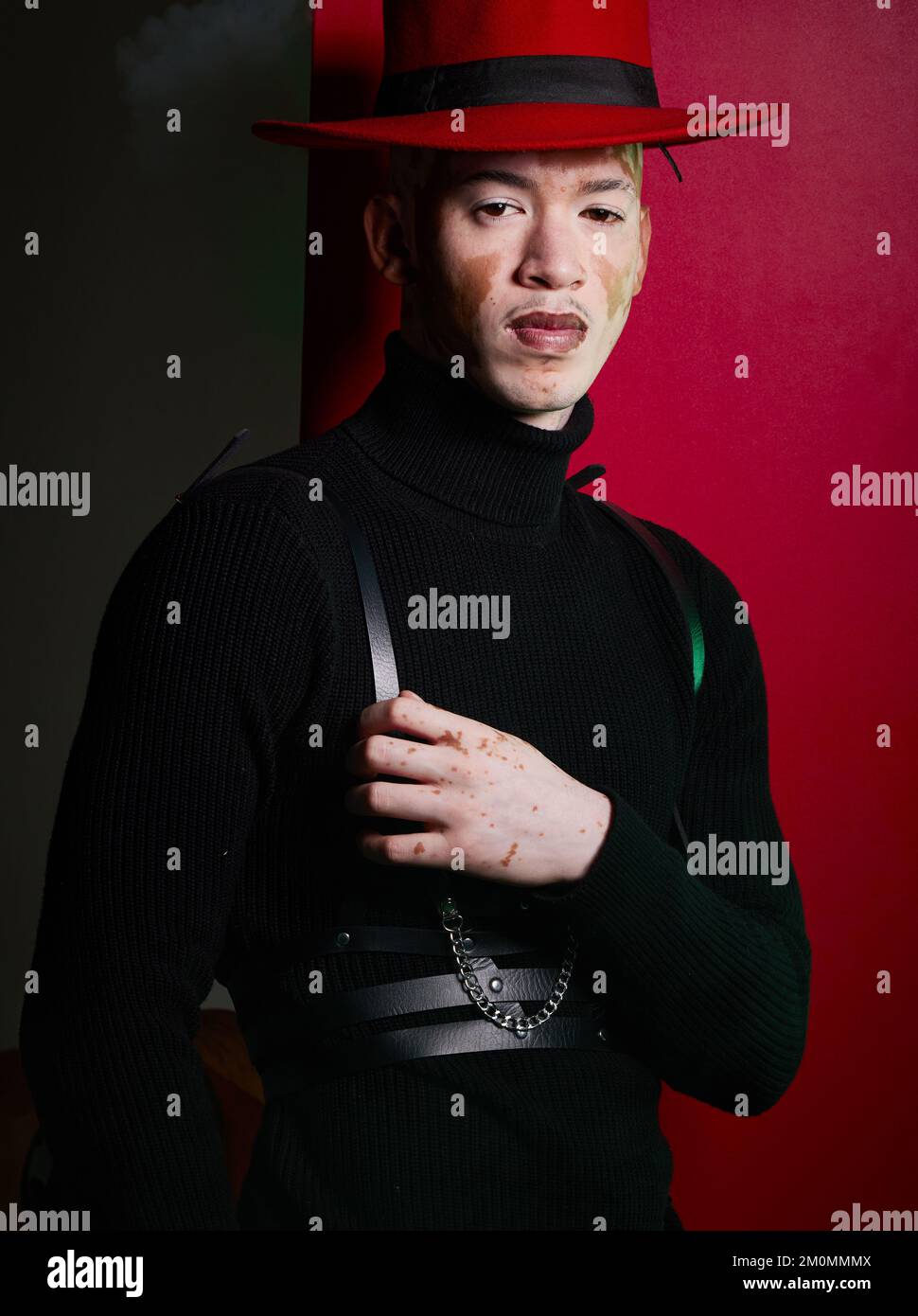 Porträt, Mode und stylischer Mann mit Vitiligo-Posen auf rotem Studiohintergrund, der selbstbewusst aussieht. Selbstvertrauen, Gesicht und trendy oder gereizter Mann Stockfoto