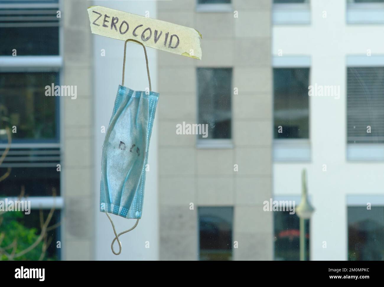 Null covid-Zeichen und alte Operationsmaske am Fenster, Bürogebäude hinten Stockfoto
