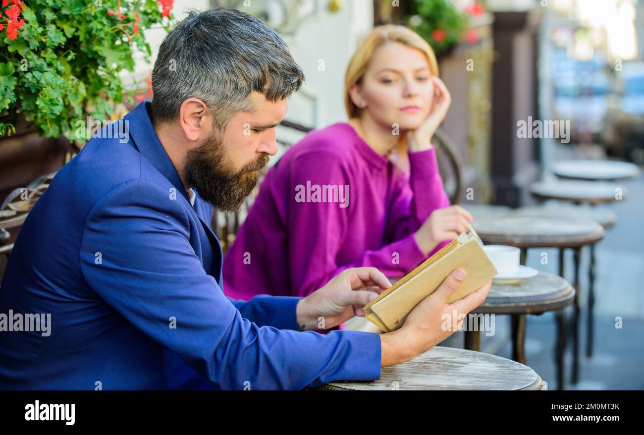Menschen mit ähnlichen Interessen treffen. Mann und Frau sitzen auf der Cafeterrasse. Das Mädchen interessiert, was er liest. Literatur von gemeinsamem Interesse. So finden Sie sie Stockfoto