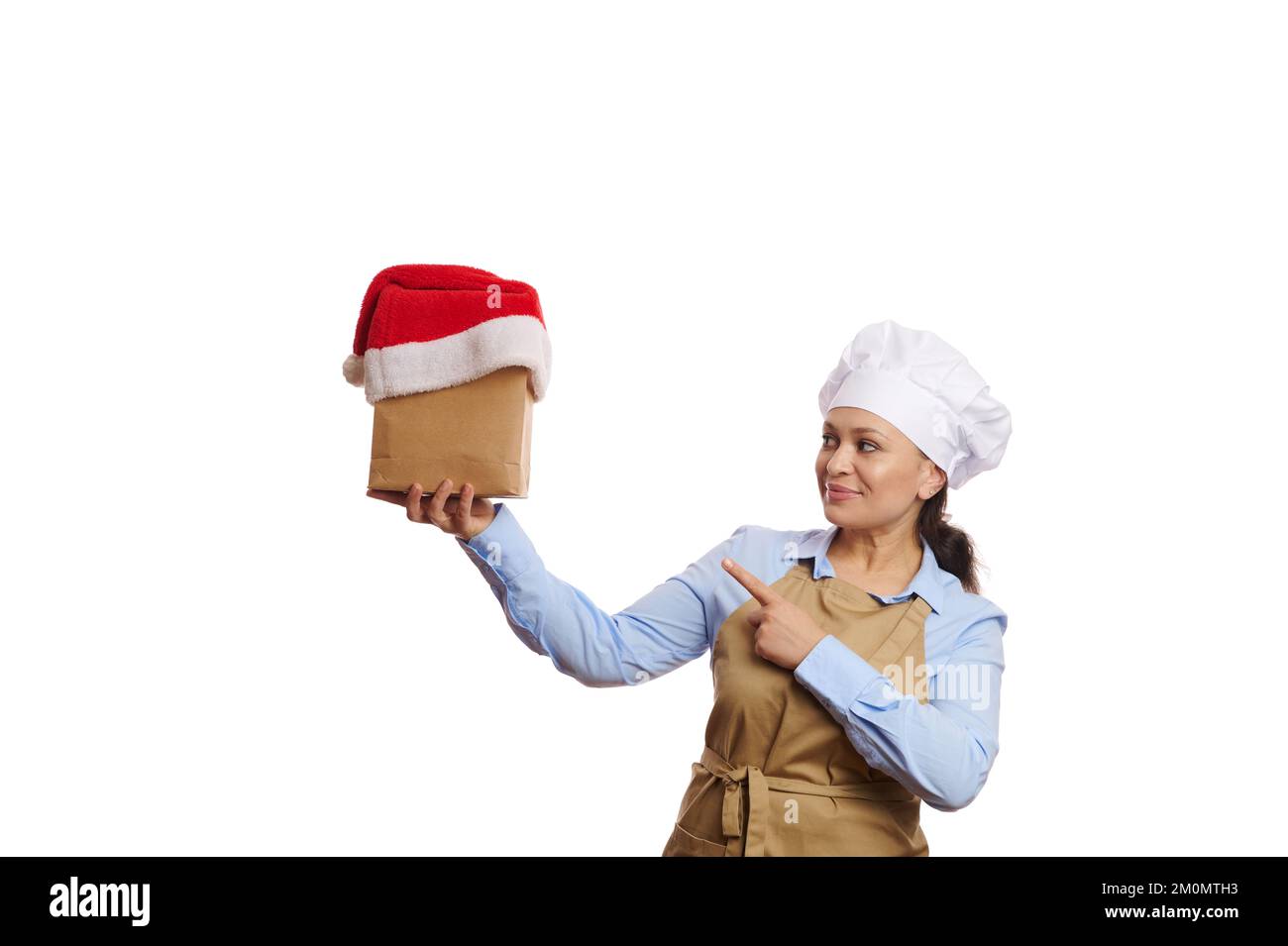 Pretty Woman Chefkoch Konditor zeigt auf Papiertüte mit Essen und Trinken, bedeckt mit Weihnachtsmannmütze. Lieferung zu Weihnachten Stockfoto