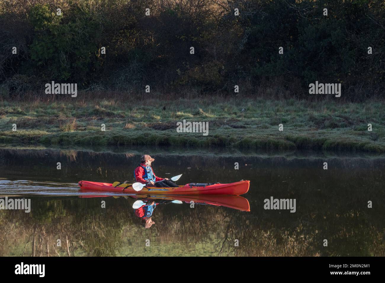 Isolierter einsamer Kanufahrer/Kajakfahrer auf dem Fluss Fowey in Lostwithiel (Cornwall) bei kaltem Sonnenlicht am frühen Morgen im Dezember. Für Outdoor-Sportarten. Stockfoto