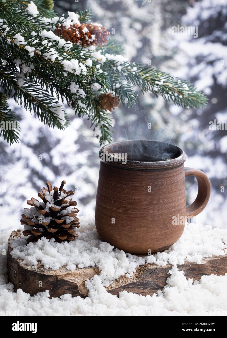 Dampfende heiße Tasse Kaffee auf einem schneebedeckten Baumstumpf mit Winterwald-Hintergrund Stockfoto