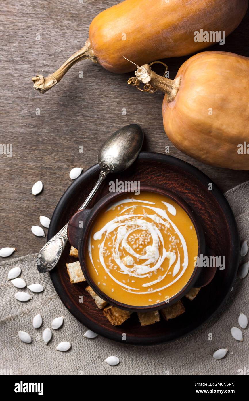 Kürbissuppe mit Creme und Sesam in brauner Keramikschale auf Holzboden. Flach liegend, Draufsicht. Stockfoto