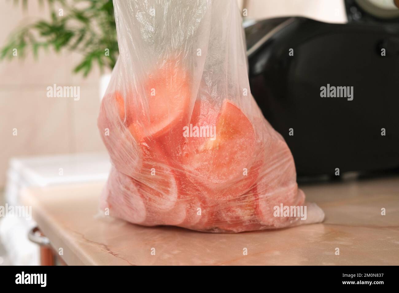 Gefrorene Tomaten, in dünne Scheiben geschnitten, in einem Zellophan-Beutel aus dem Gefrierschrank. Schnelles Kochen. Kochen von Mittagessen und Abendessen für die Familie zu Hause. Gemüsebestände für den Winter. Langzeitlagerung. Stockfoto