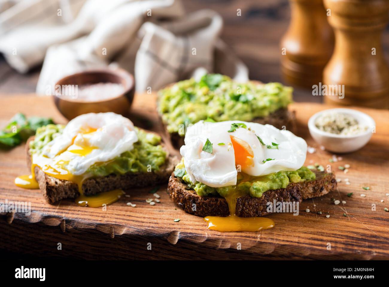 Roggentoast mit zerdrückter Avocado und pochiertem Ei auf Holzbrett, Nahaufnahme. Gesunder Avocado-Toast zum Frühstück Stockfoto