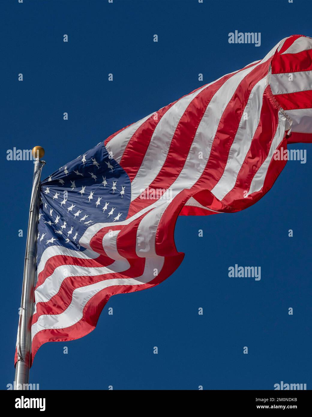 Eine große amerikanische Flagge bläst im Wind gegen einen hellblauen Himmel. Stockfoto