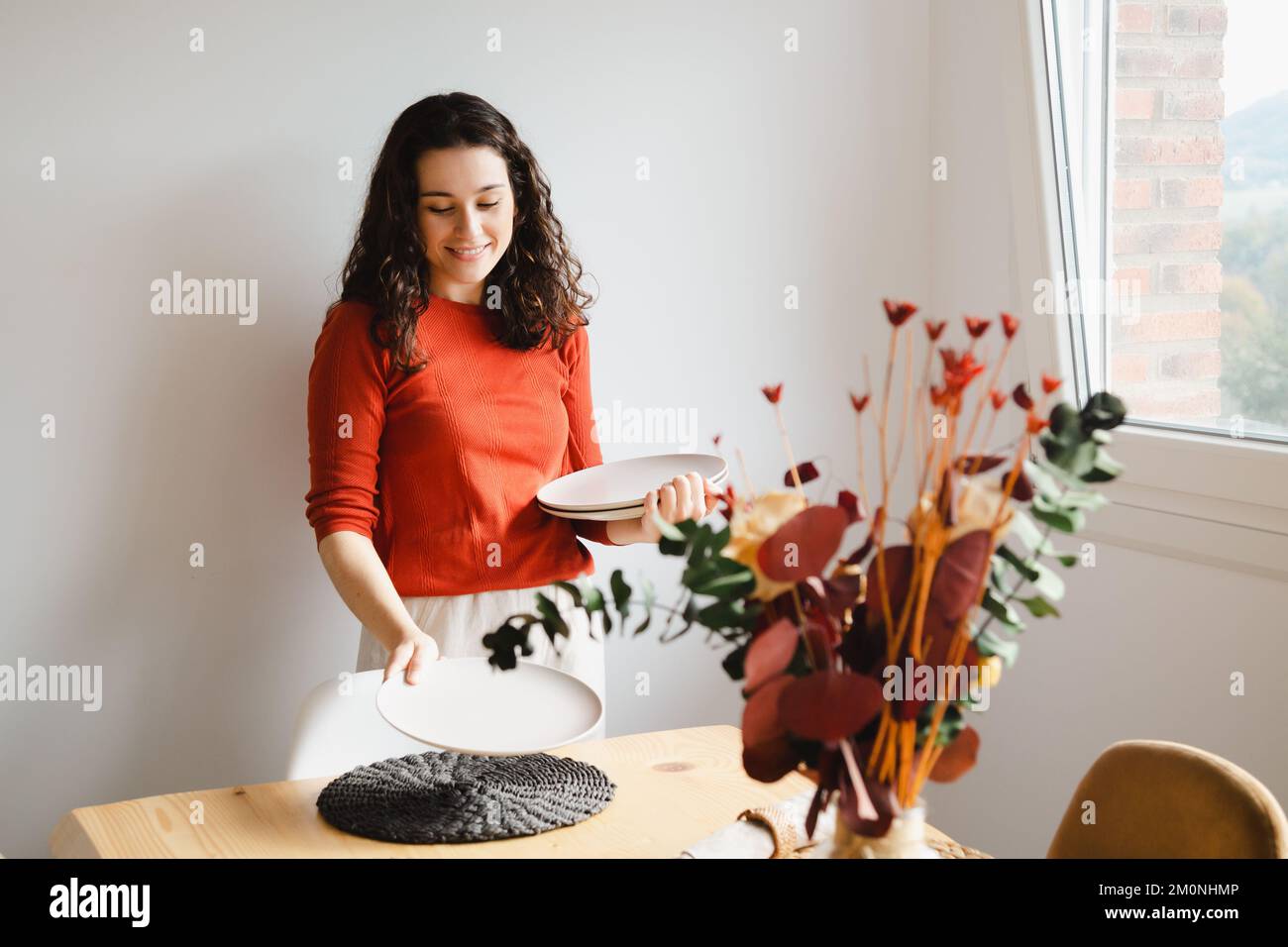 Junge, glückliche Frau, die zu Hause den Tisch für das Abendessen gedeckt hat Stockfoto