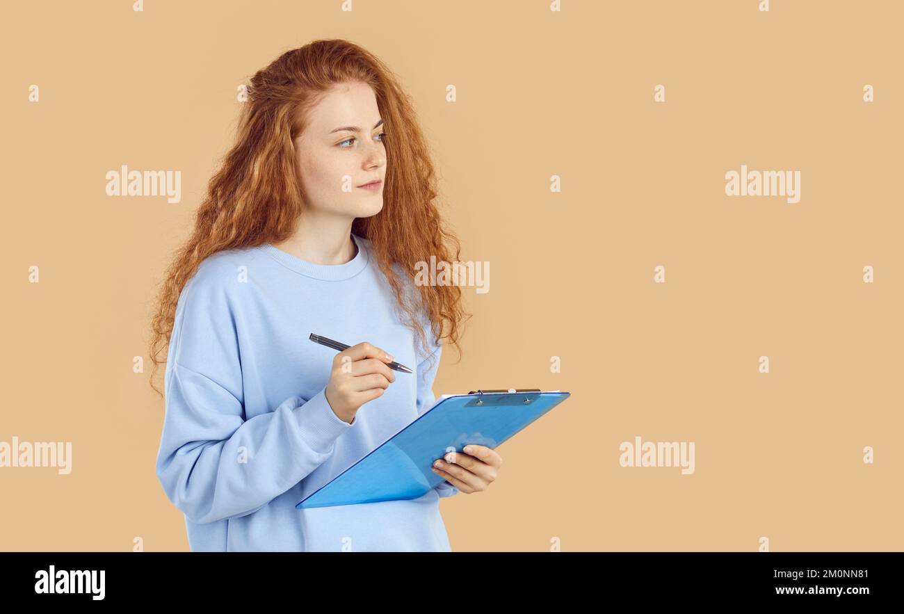 Ein Teenager hält ein Klemmbrett und denkt nach oder denkt sich Ideen für ihr Schulprojekt aus. Stockfoto