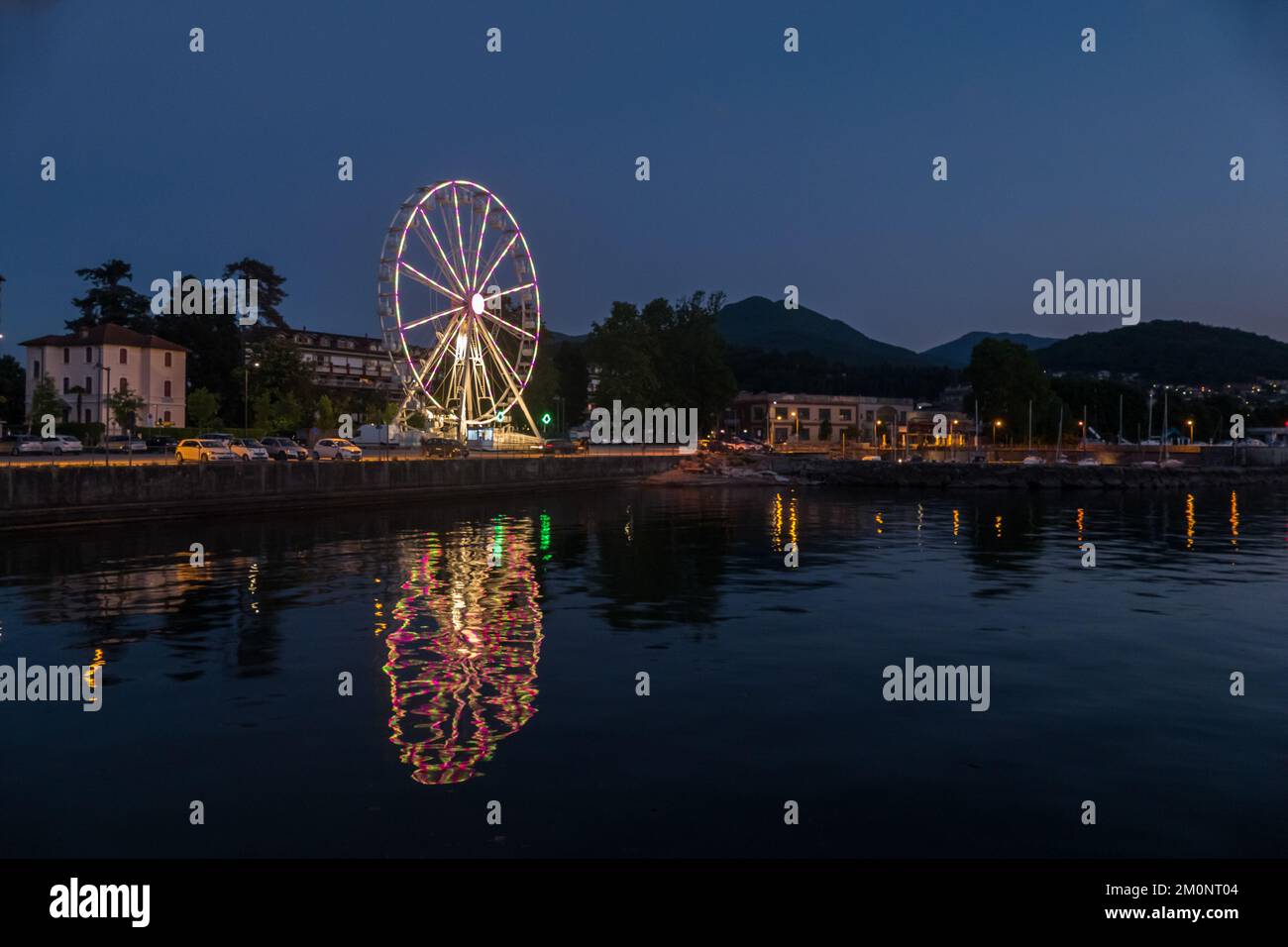 Luino, Italien: 05-18-2021: Riesenrad beleuchtet am Abend mit Lichtern, die auf dem Lago Maggiore in Luino reflektieren Stockfoto