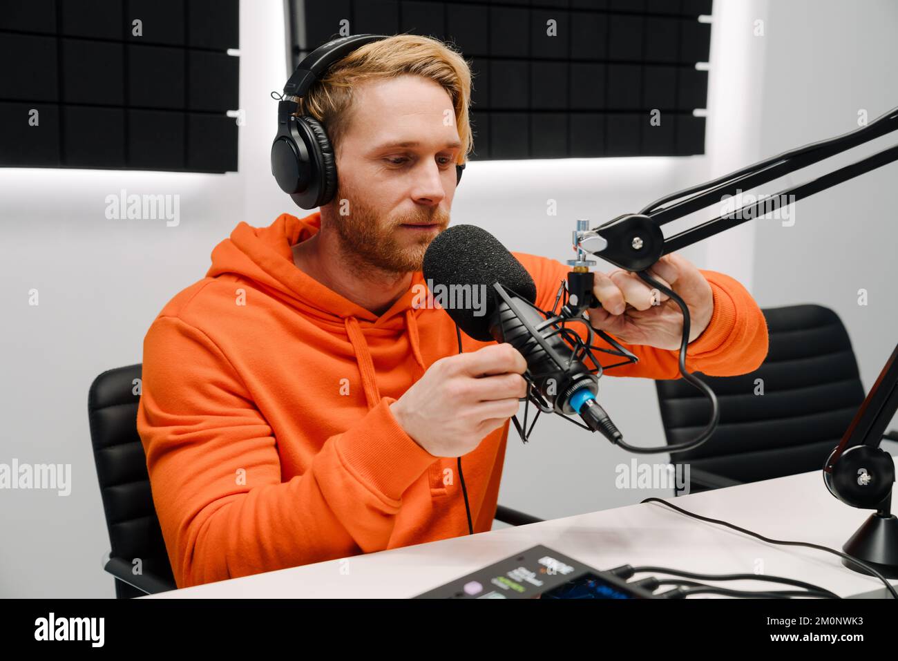 Glücklicher junger Radio-Gastgeber, der Mikrofon und Kopfhörer benutzt, während er im Studio sendet Stockfoto