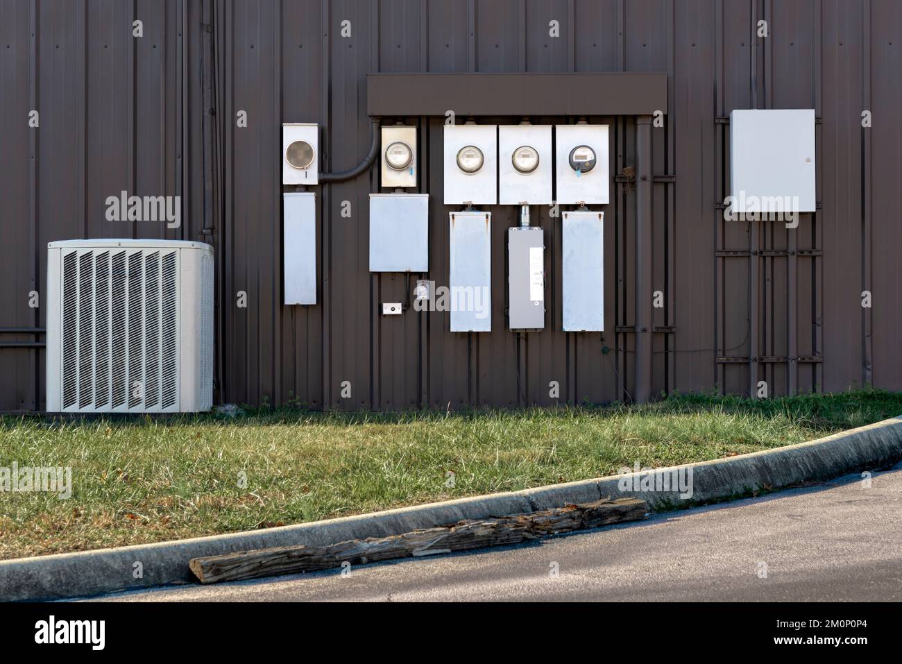 Elektrische Zähler und ein Klimakompressor außerhalb eines kleinen Bürogebäudes. Stockfoto