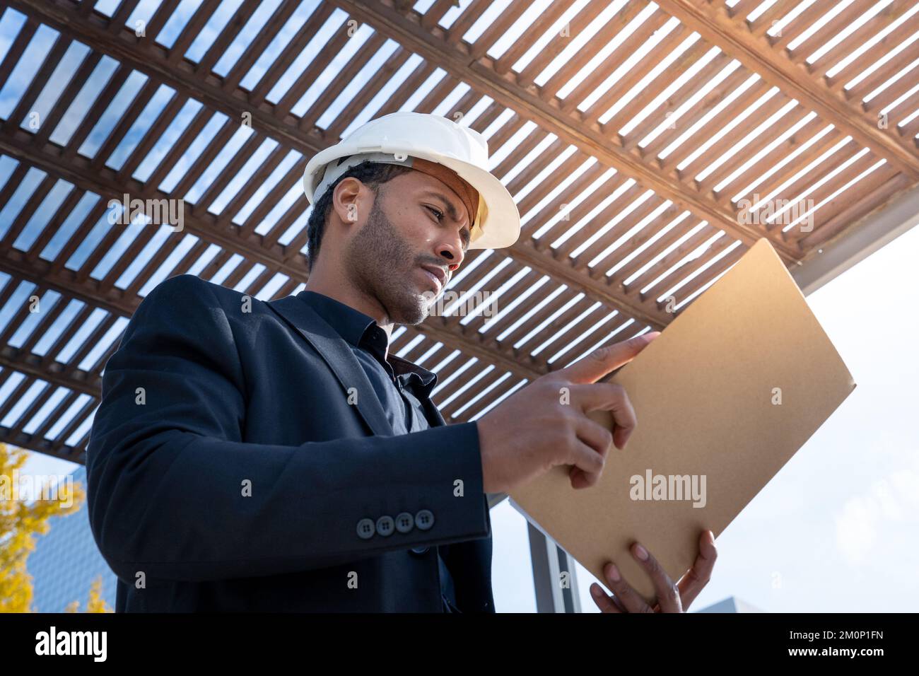 Afroamerikanischer Geschäftsführer mit Bauhelm, der die Baupläne für ein Projekt überprüft. Stockfoto