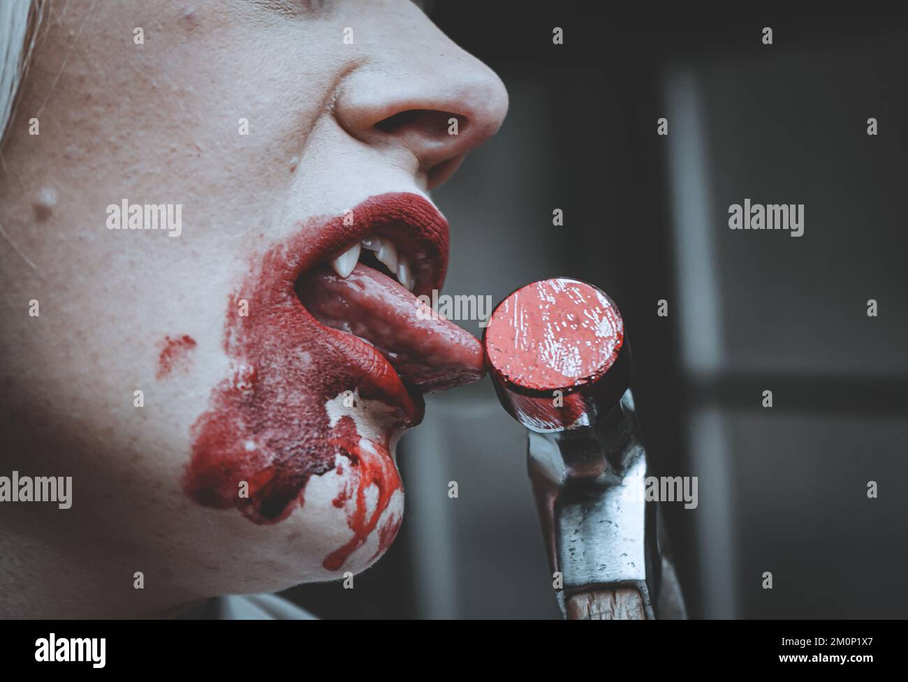 Nahaufnahme eines weiblichen Vampirs, der blutigen Hammer leckt Stockfoto