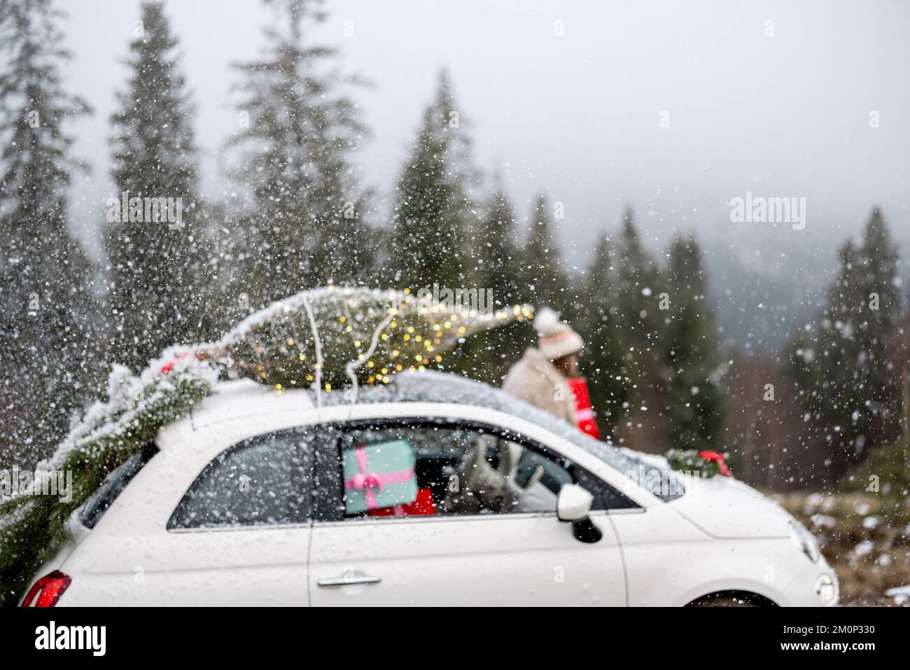 Frau fährt mit dem Auto mit Geschenken und Weihnachtsbaum auf der Bergstraße Stockfoto